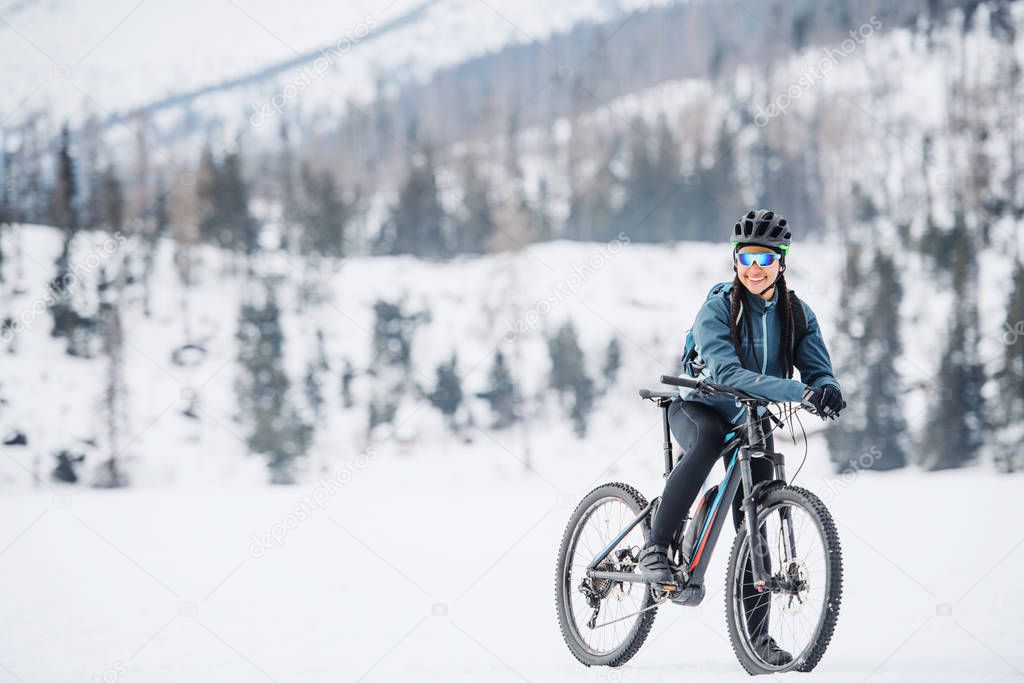 Female mountain biker with bicycle standing outdoors in winter nature.