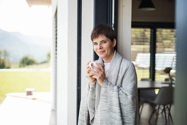 Una joven con café de pie junto a la puerta del patio en casa . — Foto de Stock