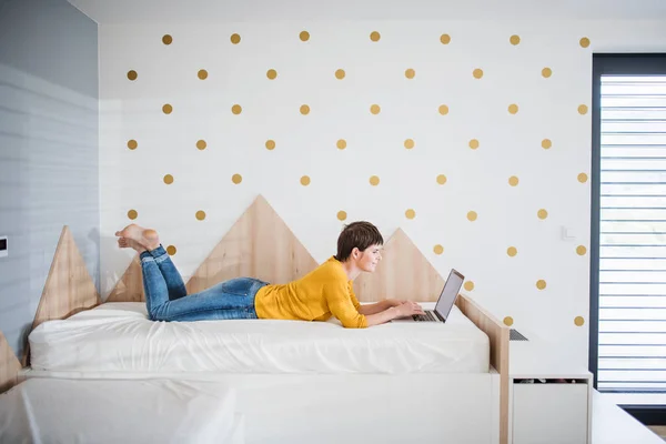 Jonge vrouw met laptop liggend op bed in slaapkamer binnen thuis. — Stockfoto