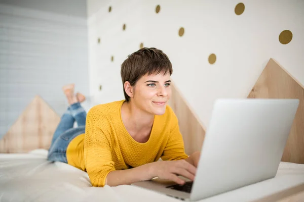 Jovem com laptop deitado na cama no quarto dentro de casa . — Fotografia de Stock