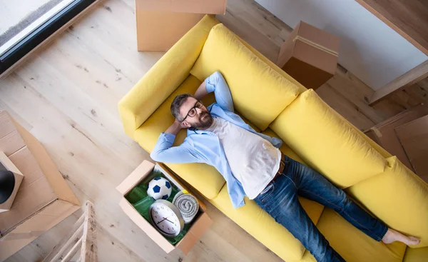 Vue du dessus de l'homme mûr avec des boîtes se déplaçant dans une maison neuve, détente sur canapé . — Photo