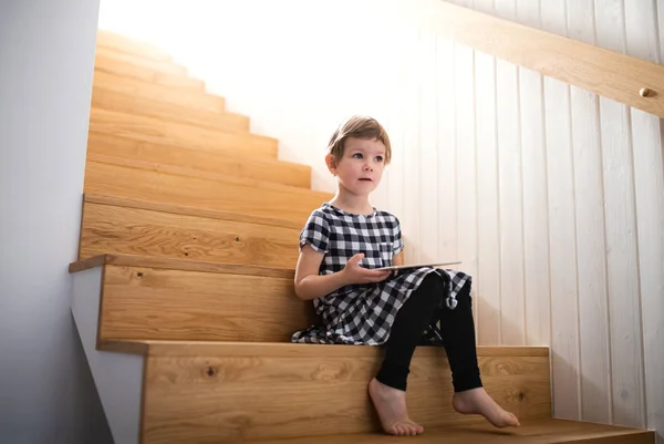 Une petite fille assise à l'intérieur dans les escaliers, en utilisant une tablette . — Photo