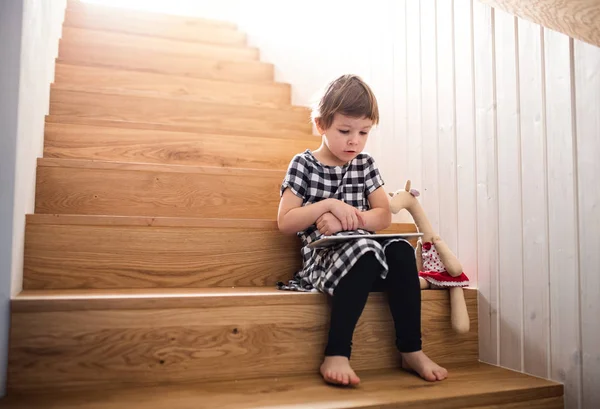 Ein kleines Mädchen sitzt drinnen auf der Treppe und benutzt Tabletten. — Stockfoto
