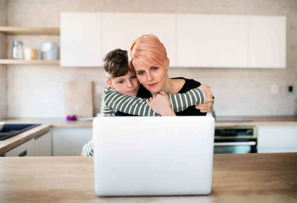 Una giovane donna con un piccolo figlio che usa il computer portatile in cucina a casa . — Foto Stock