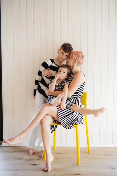 Kobieta z dwójką dzieci w czarno-białych ubraniach przeciwko białej drewnianej ścianie. — Zdjęcie stockowe