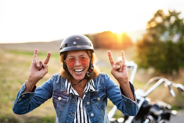 Una alegre viajera senior con moto en el campo al atardecer . —  Fotos de Stock