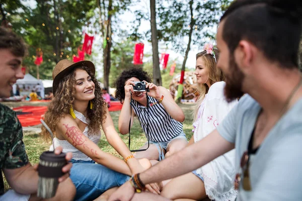 Group of young friends sitting on ground at summer festival, taking photo. — Stock Photo, Image