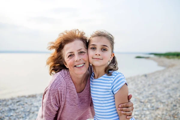Büyükannesiyle gölün kenarında küçük bir kız, kameraya bakıyor.. — Stok fotoğraf