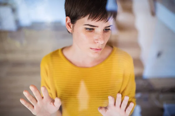 Vista frontale di triste giovane donna in piedi in casa, mani su vetro . — Foto Stock