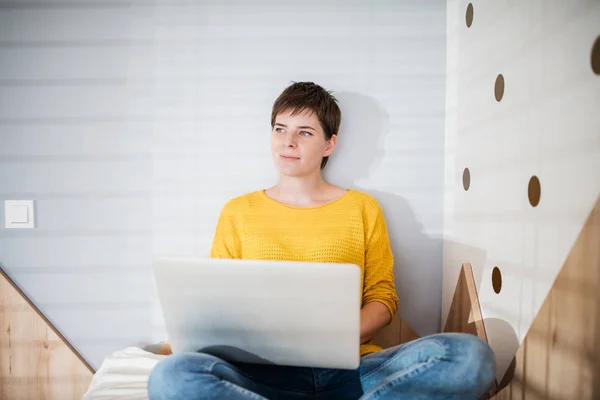 Jeune femme avec ordinateur portable assis sur le lit dans la chambre à coucher à l'intérieur à la maison . — Photo