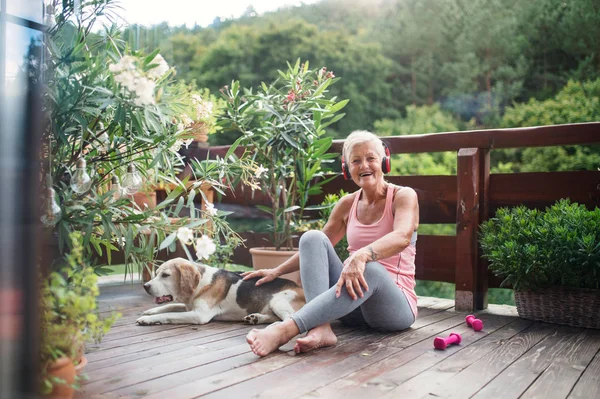 A senior woman with headphones outdoors on a terrace, resting after exercise. — Stockfoto