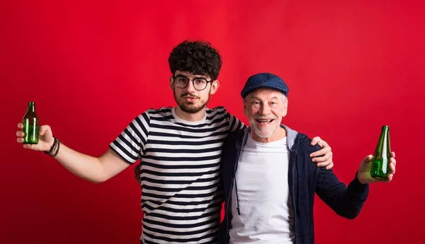 Giovane e padre anziano con bottiglie in uno studio su sfondo rosso . — Foto Stock