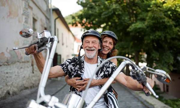 Ein fröhliches Seniorenpaar mit Motorrad in der Stadt unterwegs. — Stockfoto