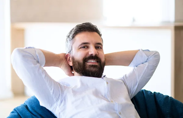 Felice uomo maturo che si muove nella nuova casa non arredata, seduto sul sacchetto di fagioli . — Foto Stock