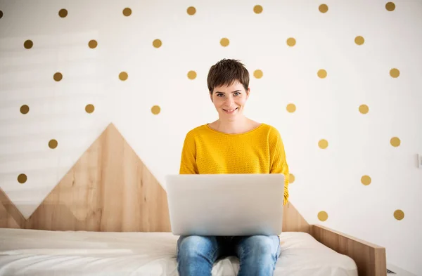 Jonge vrouw met laptop zittend op bed in de slaapkamer binnen thuis. — Stockfoto