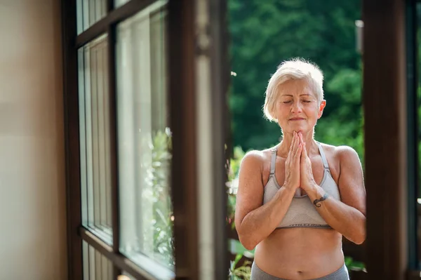 Een oudere vrouw die in de zomer buiten op een terras staat, yoga doet. — Stockfoto