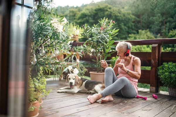 A senior woman with headphones outdoors on a terrace, resting after exercise. — Stockfoto