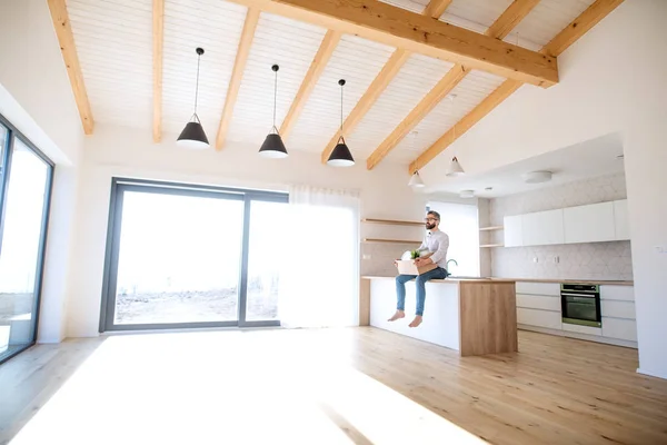 Mature homme assis dans une maison non meublée, tenant une boîte de déménagement . — Photo