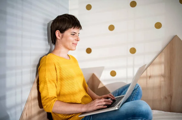 Jovem mulher com laptop sentado na cama no quarto dentro de casa . — Fotografia de Stock