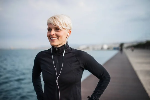 Porträt einer jungen Sportlerin mit Kopfhörern, die draußen am Strand steht. — Stockfoto