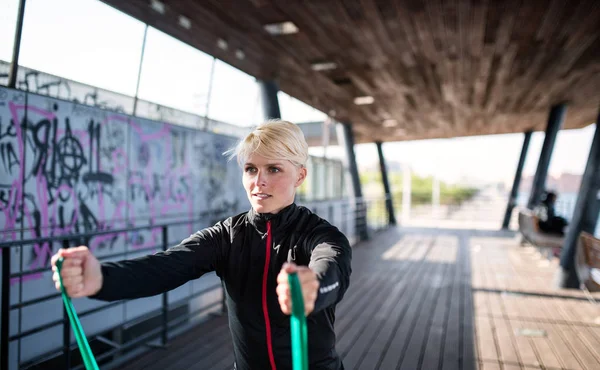 Eine junge Sportlerin mit Gummibändern beim Sport im Freien in der Stadt. — Stockfoto