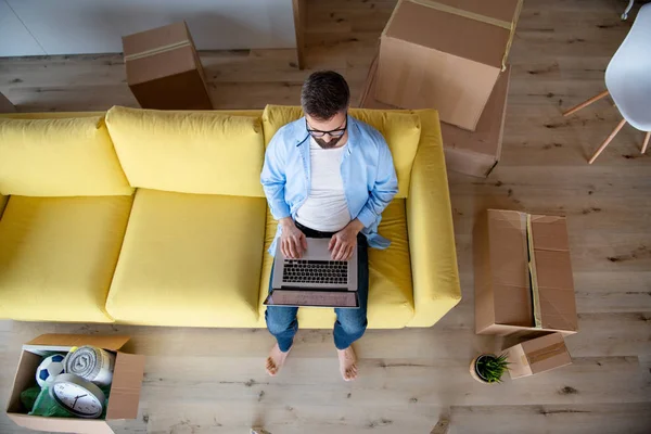 Ovanifrån av mogen man sitter på soffan i omöblerat hus, med hjälp av laptop. — Stockfoto