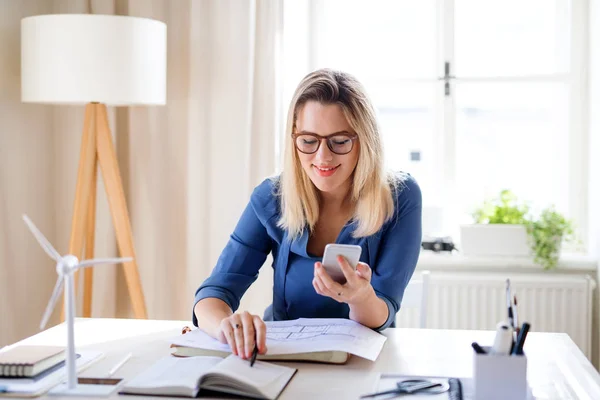 Jeune femme architecte assise au bureau à l'intérieur dans le bureau à la maison, travaillant . — Photo