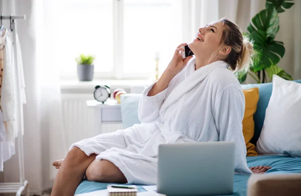 Jovem mulher com telefone e laptop na cama dentro de casa pela manhã . — Fotografia de Stock