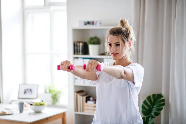 Young woman with dumbbells doing exercise in bedroom indoors at home. — 스톡 사진
