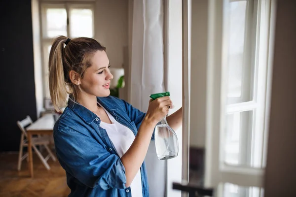 Junge Frau steht zu Hause drinnen und putzt Fenster. — Stockfoto