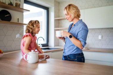 A cute small girl with mother indoors in kitchen at home. clipart