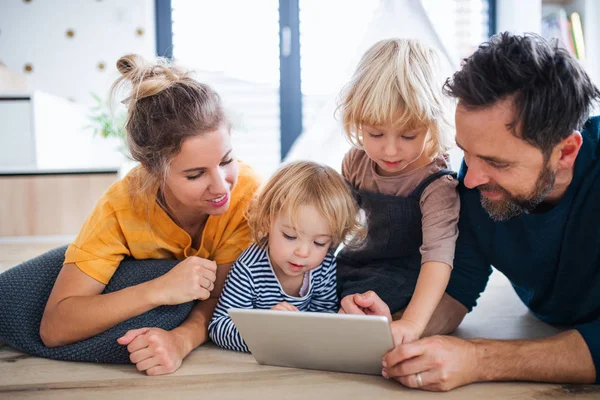 Jeune famille avec deux jeunes enfants à l'intérieur dans la chambre, en utilisant une tablette . — Photo