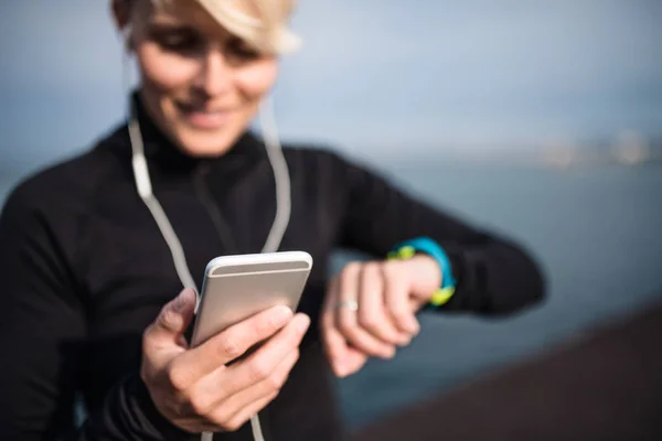 Молодая спортсменка со смартфоном стоит на открытом воздухе на пляже . — стоковое фото