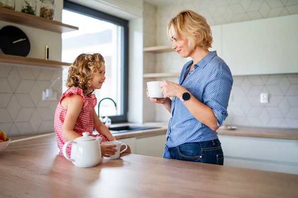 Una piccola ragazza carina con madre al chiuso in cucina a casa . — Foto Stock
