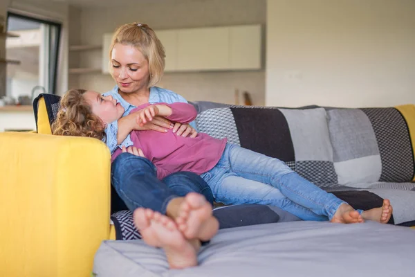 Une jolie petite fille avec une mère sur le canapé à l'intérieur à la maison, se reposant . — Photo