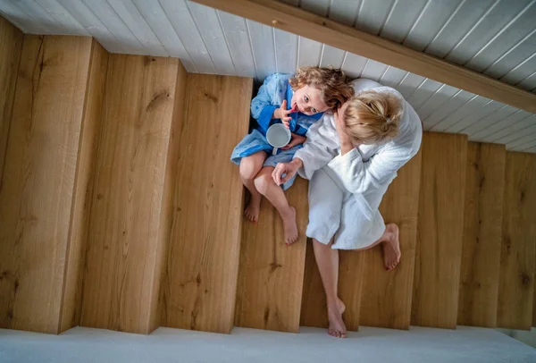 Top view of small girl with mother indoors at home, sitting on stairs in the morning. — Stock Photo, Image