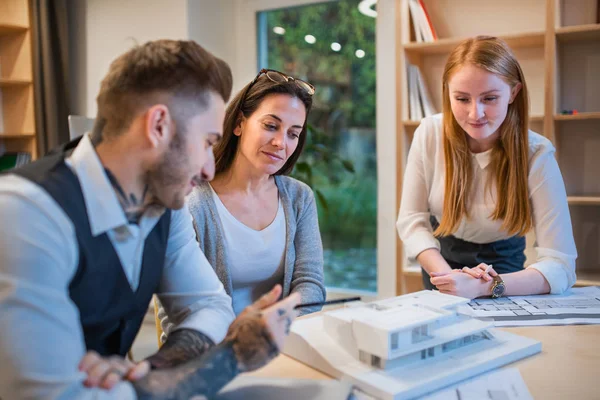 Grupo de arquitectos con modelo de casa sentada en interiores en oficina, trabajando . — Foto de Stock