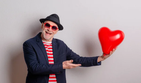 Портрет старшого коханого чоловіка в студії, що тримає червону кульку серця . — стокове фото