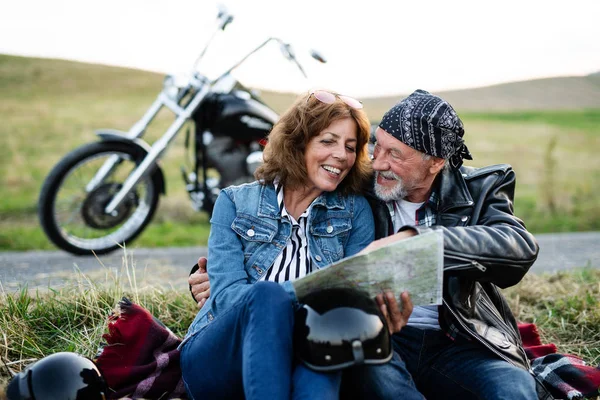 Veselý starší pár cestovatelů s mapou a motocykl na venkově. — Stock fotografie