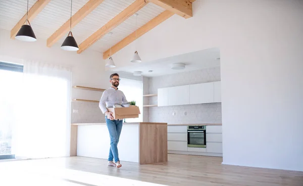 Homme mûr marchant dans une maison non meublée, tenant une boîte de déménagement . — Photo