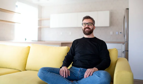 Cheerful mature man sitting on sofa in unfurnished house. — ストック写真