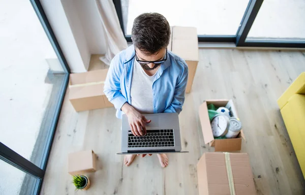 Κάτοψη του ώριμου άντρα με τα κουτιά να κινούνται σε νέο σπίτι, χρησιμοποιώντας laptop. — Φωτογραφία Αρχείου
