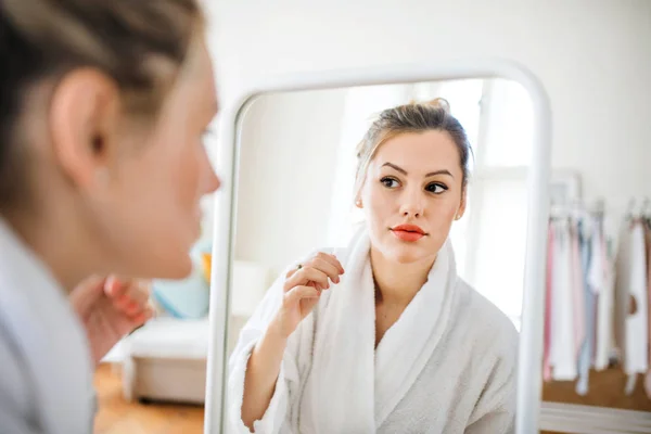 Ung kvinna inomhus på morgonen, tittar i spegeln. — Stockfoto