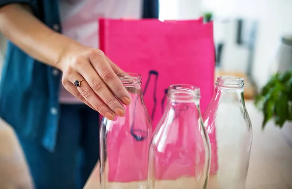 Giovane donna mettendo bottiglie di vetro in borsa in casa, concetto di riciclaggio . — Foto Stock