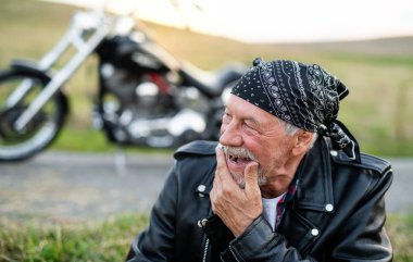 Neşeli, kıdemli bir gezgin motosikletle kırsalda dinleniyor..