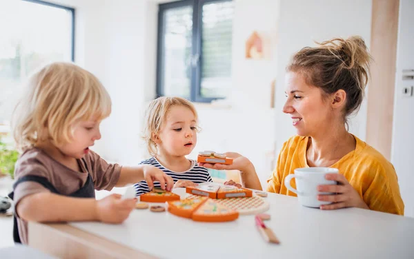 Mother with two small children indoors in bedroom playing with toys. — Stock Photo, Image