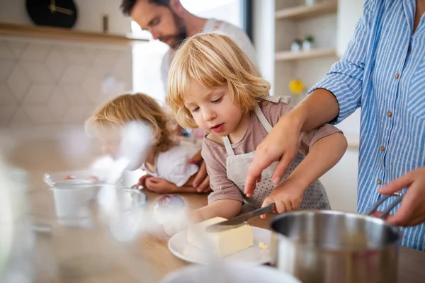 Молода сім'я з двома маленькими дітьми в приміщенні на кухні, готуючи їжу . — стокове фото