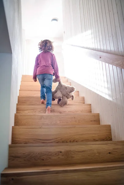 Una vista trasera de una niña pequeña subiendo escaleras de madera en el interior de casa . — Foto de Stock