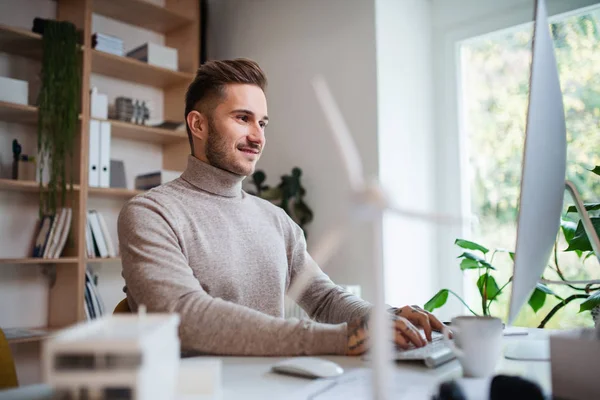 Ung affärsman sitter vid skrivbordet inomhus på kontoret, med hjälp av dator. — Stockfoto