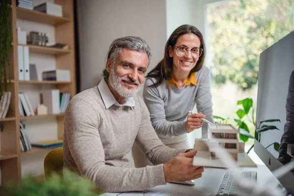 Architecten met model van het huis zitten aan de balie binnen in kantoor, werken. — Stockfoto